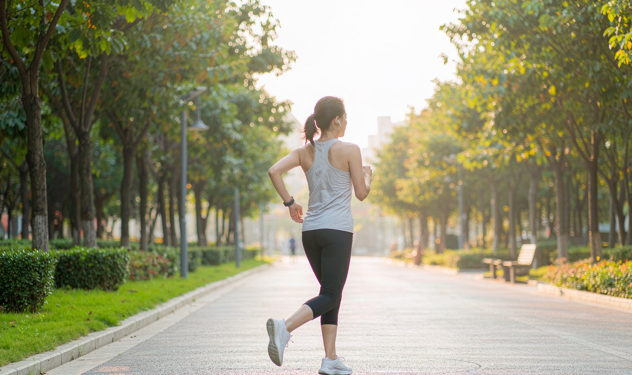 A woman jogging along a tree-lined park path in soft golden morning light